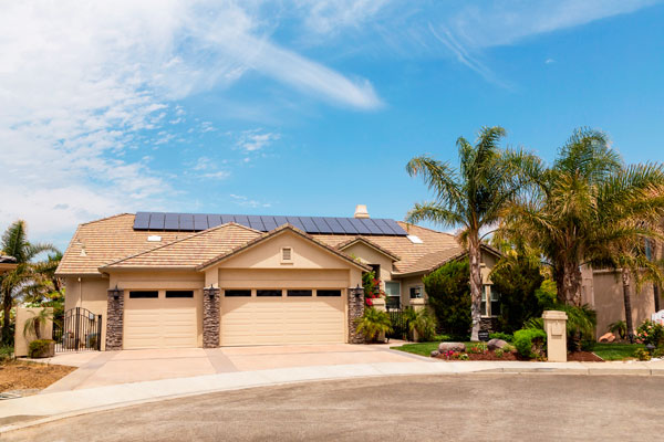 Tan home with solar panels on the roof and palm trees in the front yard