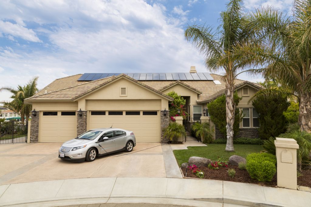 Tan home with palm trees in the front yard, a blue sky, and solar panels on the roof