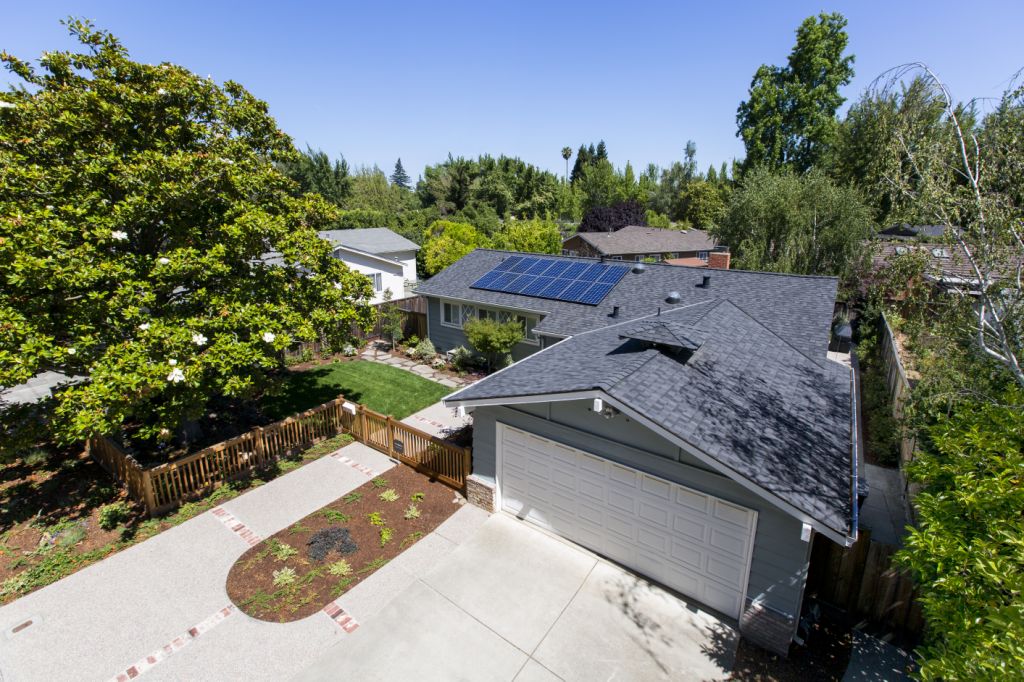 Arial shot of a grey house with a large driveway and solar panels on the roof